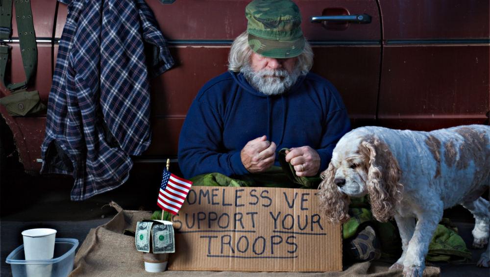 veteran sitting with sign to support homeless vets