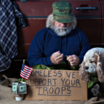 veteran sitting with sign to support homeless vets